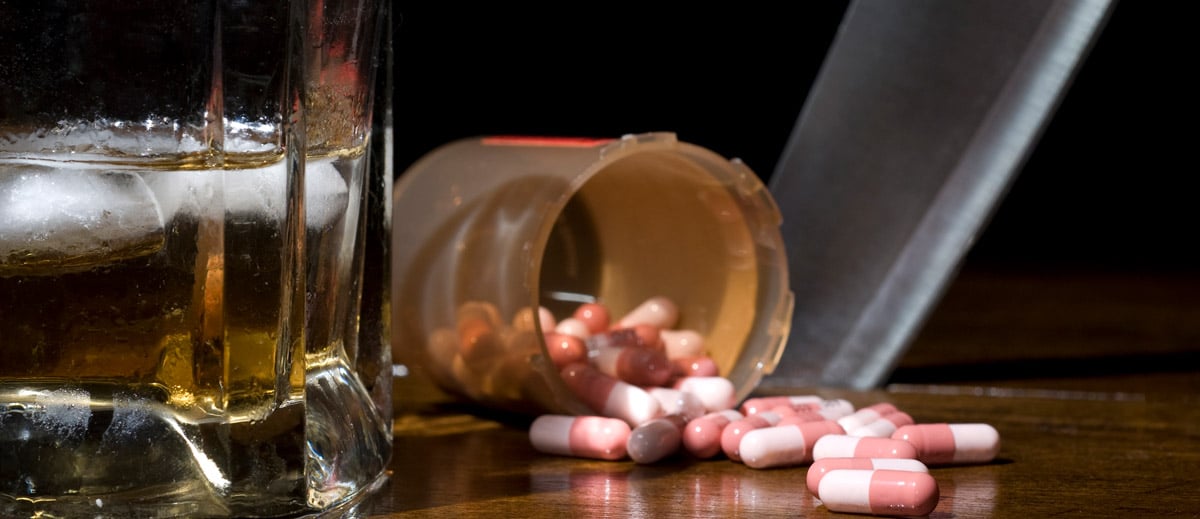 Spilled pills and a glass of alcohol side by side on a table, illustrating the dangerous risk of combined overdose.