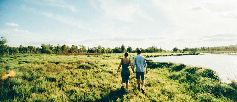Man and woman walking hand-in-hand through a sunny lakeside field, symbolizing clarity and renewal after stopping alcohol use.