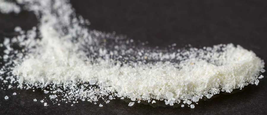 Close-up of white crystalline powder on a dark surface, representing synthetic bath salts and stimulant abuse risk.