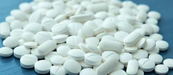A scattered pile of white prescription pills on a light background, representing opioid medications such as oxycodone and hydrocodone.