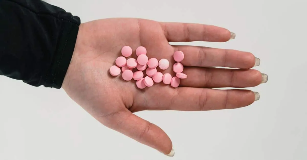 A close-up of a hand holding pink pills, highlighting addiction and healthcare themes.