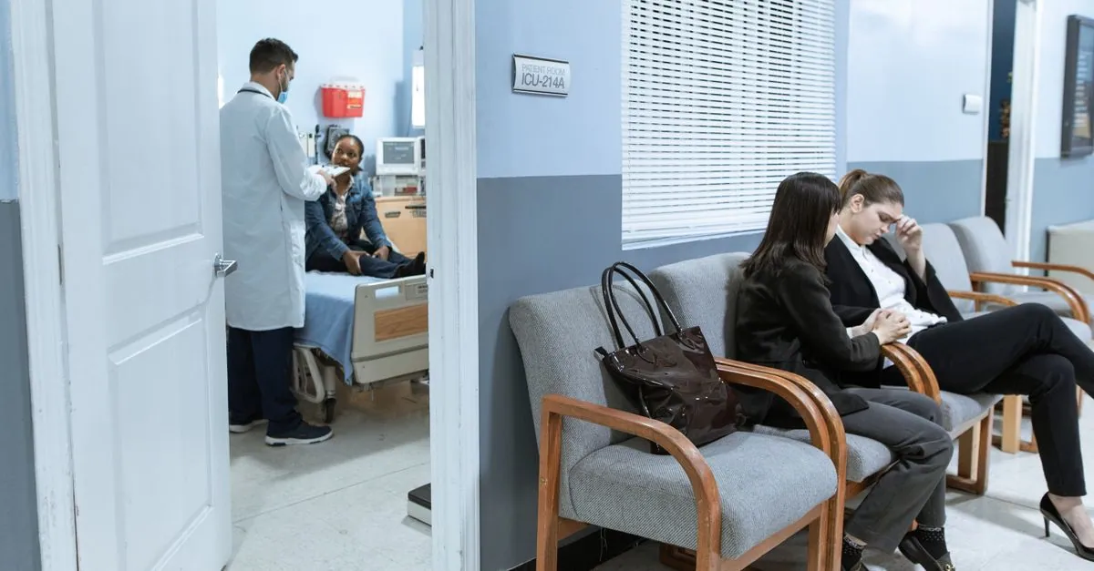 Doctor with patient in ICU, women in waiting area showing concern.