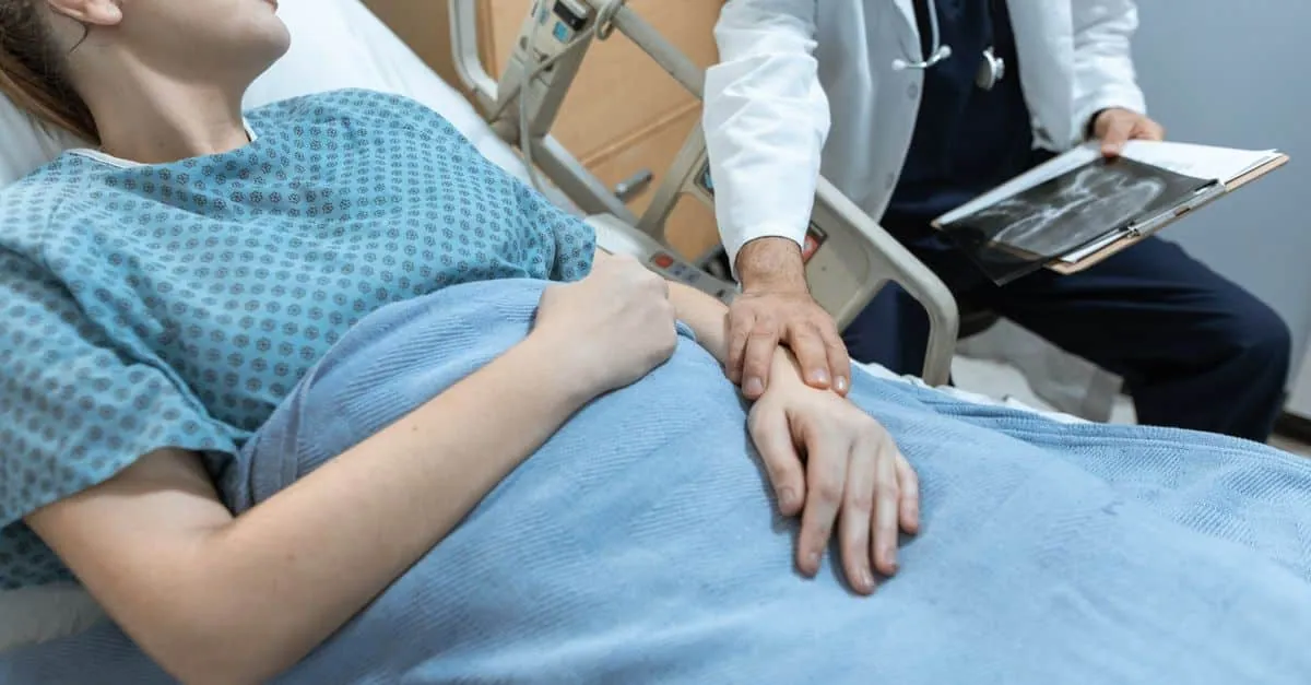 A doctor comforts a female patient in a hospital bed, holding her hand, with x-ray results.